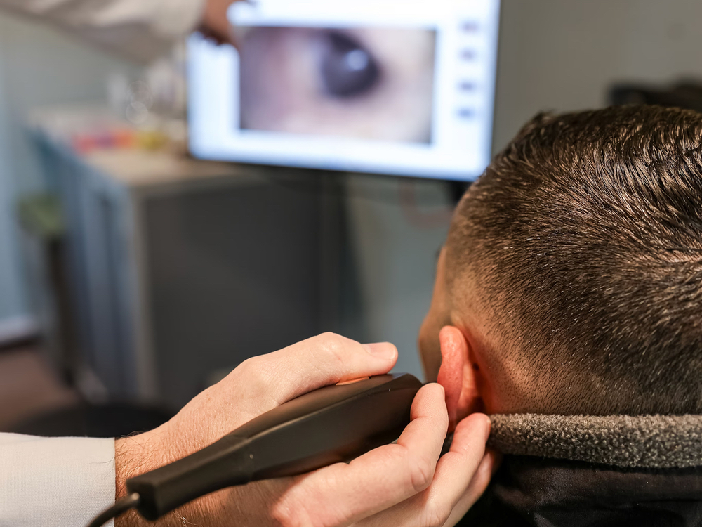 Doctor of Audiology examining a patient's ear canal before professional earwax removal at Advanced Hearing Technology in Naples, FL
